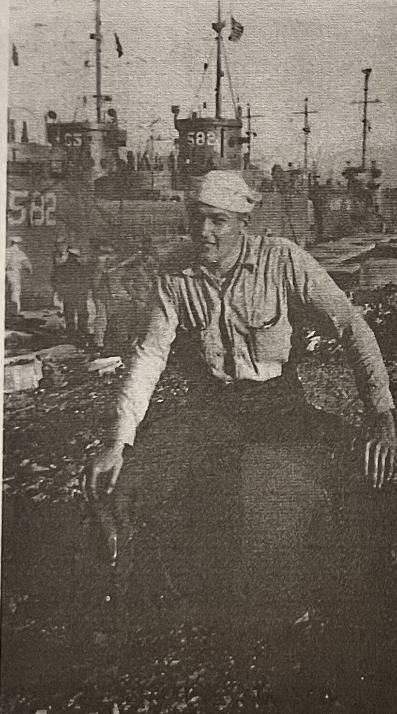 Robert Joseph Ascherl in Navy uniform in 1944, seated in front of a row of moored LCI landing craft in the Mediterranean.